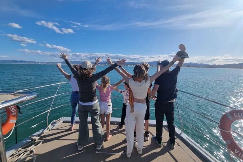 A group of people on a boat with their arms raised, facing a body of water and a distant shoreline. 4