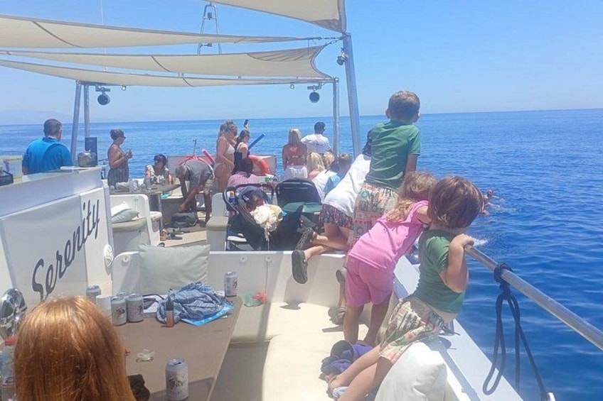 A boat with people on board, some standing and some sitting, with a clear blue sea in the background. 3