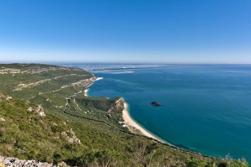 A coastal landscape with a curved shoreline, a small island, and a clear blue sky. 1