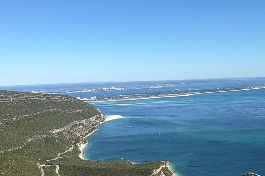 A coastal landscape with a clear blue sea, a sandy beach, and a hilly terrain with vegetation. 1