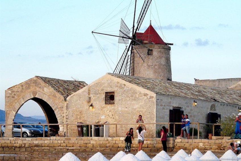 A historic stone building with a windmill, a stone archway, and people walking by. 3