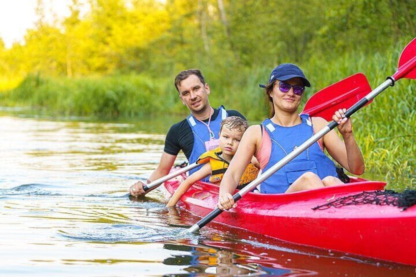 A family in a red kayak on a calm river surrounded by greenery. 1