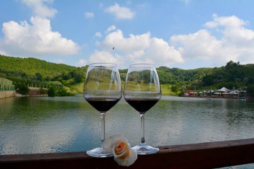 Deux verres à vin posés sur une rambarde en bois, avec un lac et des collines en arrière-plan. 3