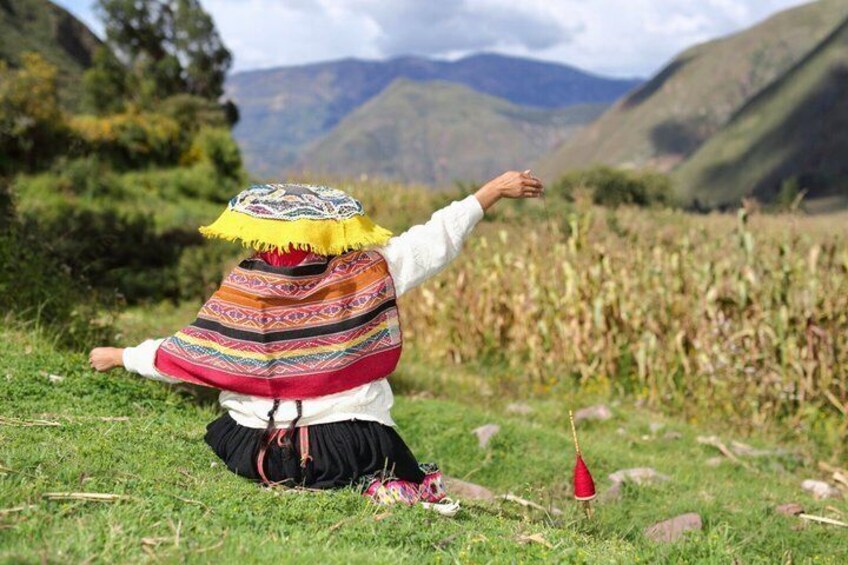 A person in traditional attire sitting on grass with mountains in the background. 5
