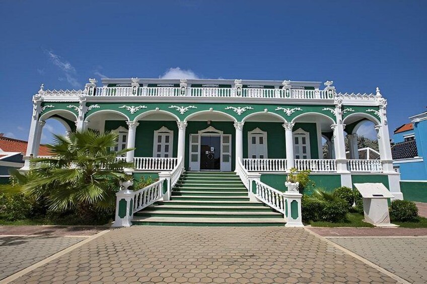 A green and white colonial-style building with a staircase leading to the entrance. 3