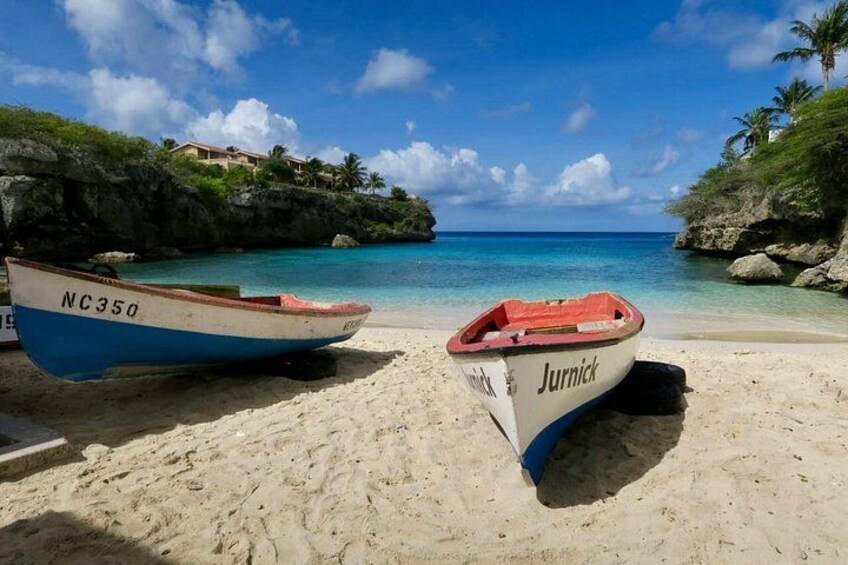 Two boats on a sandy beach with clear turquoise water and a rocky shoreline. 2