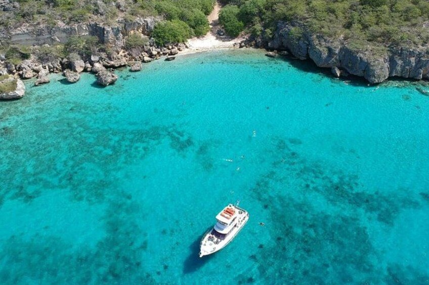 Een boot op turquoise water, omringd door rotskliffen en een strand. 2