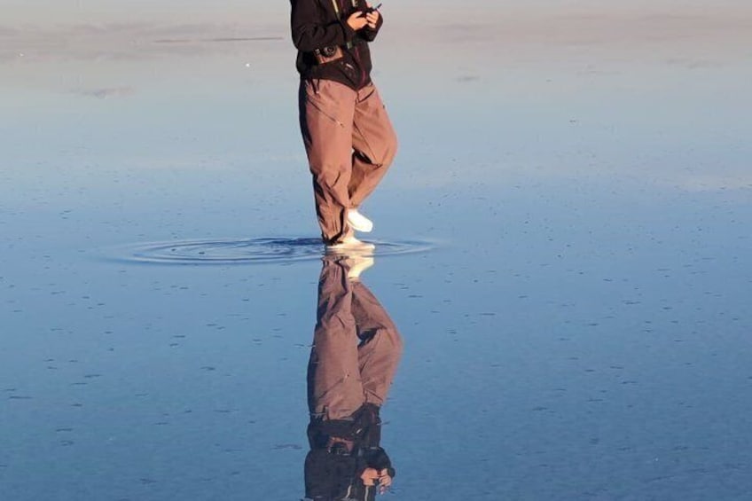 A person standing on a reflective surface, possibly water, with a clear reflection visible. 3