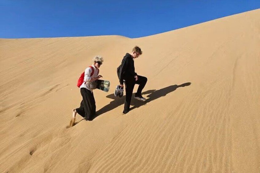 Two people climbing a sand dune with a clear blue sky. 5