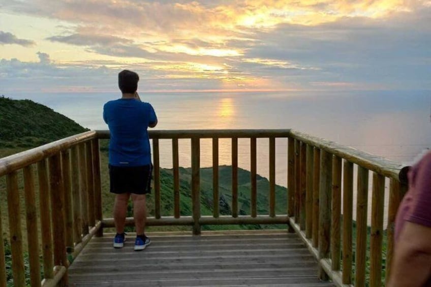A person standing on a wooden deck overlooking a body of water during sunset. 1