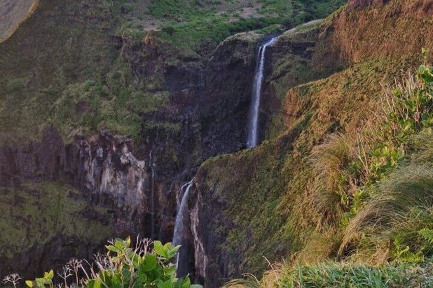 A waterfall cascading down a steep cliff surrounded by lush greenery. 2