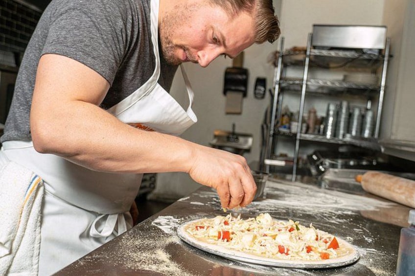 A person in a kitchen preparing food, with a pizza on the counter and various kitchen items in the background. 4