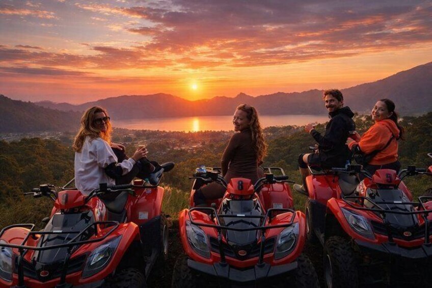 Four people on ATVs overlooking a sunset with mountains in the background. 1