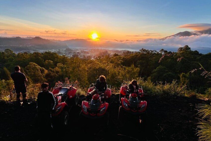 A sunset over a mountainous landscape with people on a red ATV. 3