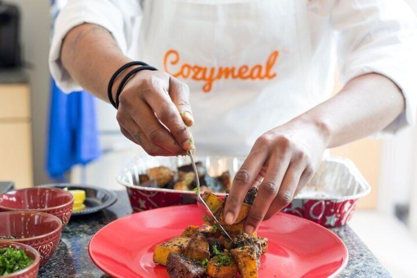 A person in a white apron with 'Cozymmeal' text preparing food on a red plate. 2