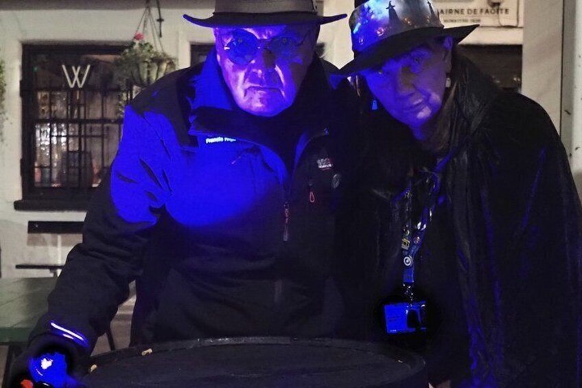 Two individuals in dark clothing and hats, one holding a device with a blue light. 4