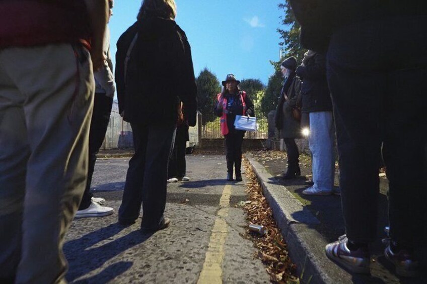 A group of people standing on a sidewalk, some holding papers. 3
