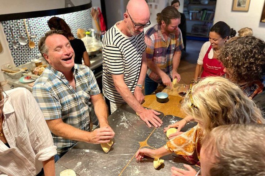 Un grupo de personas participa en una actividad de cocina, hay harina en la mesa y alguien está estirando masa. 2