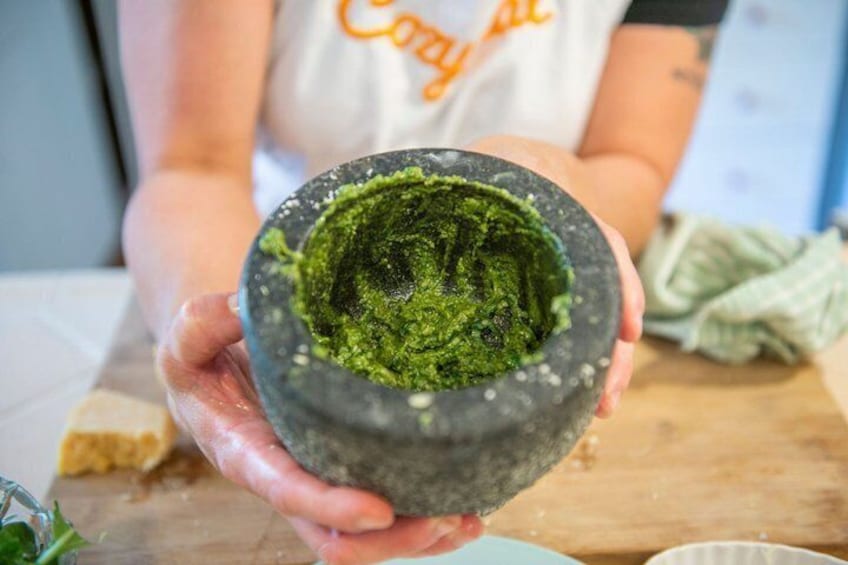 A person holding a mortar with green contents, likely a herb paste, on a kitchen counter. 3