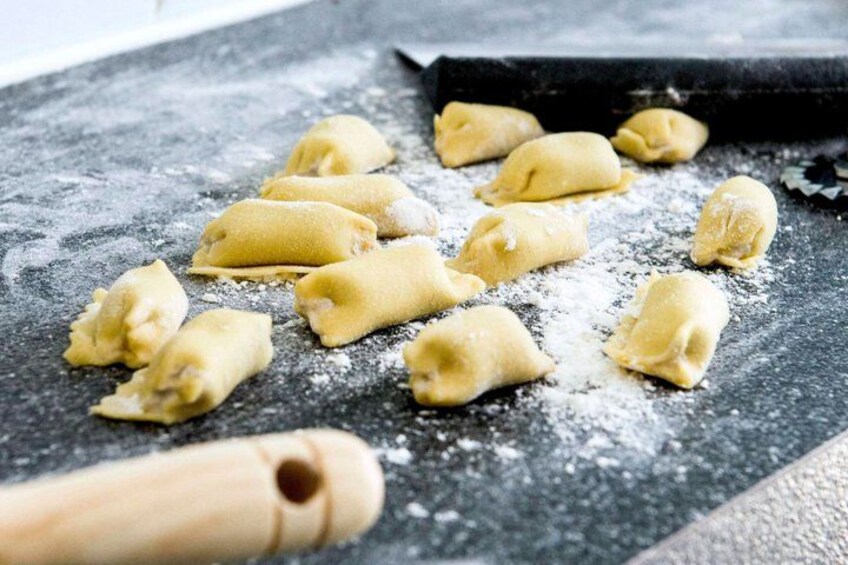 Uncooked pasta on a floured surface with a rolling pin and a pasta cutter nearby. 2