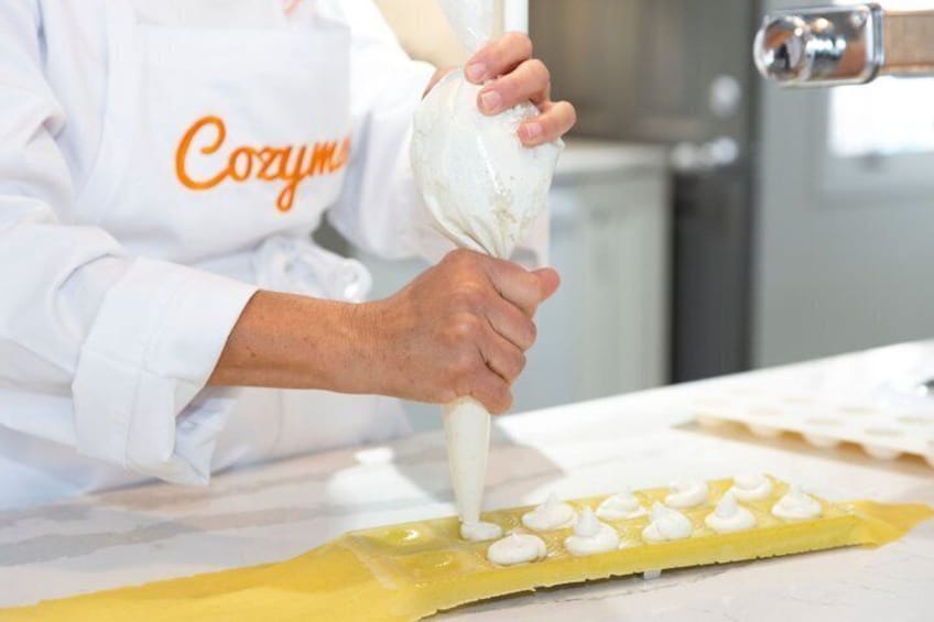 A person in a white chef's coat with 'Cozym' on it, piping cream onto a yellow pastry. 1