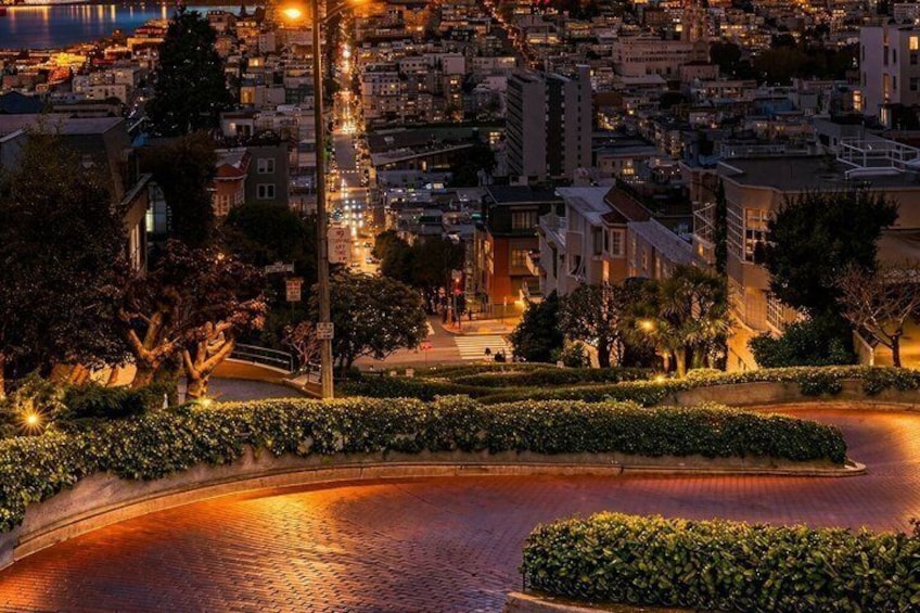 A nighttime cityscape with a curved road, illuminated buildings, and a body of water. 4
