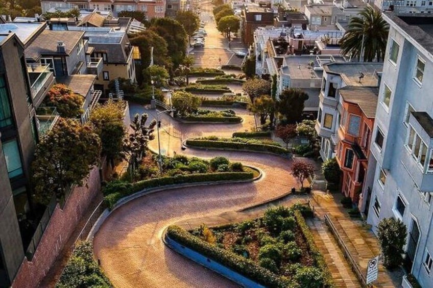A winding road through a residential area with houses on both sides, surrounded by greenery and trees. 3