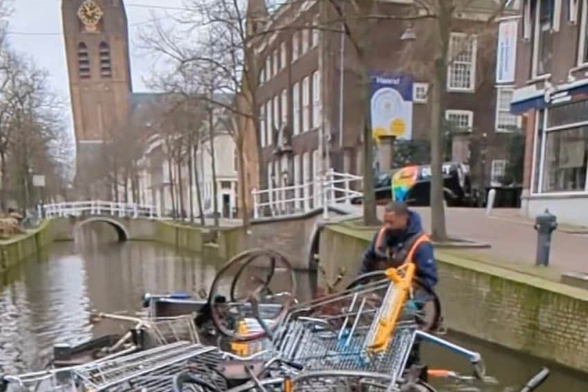 A canal with a bridge, a clock tower, and a person pushing a cart with bicycles. 3