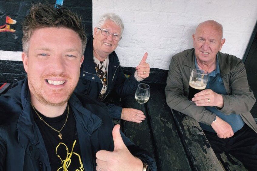 Three people sitting on a bench, one giving a thumbs-up, and holding glasses of beer. 2