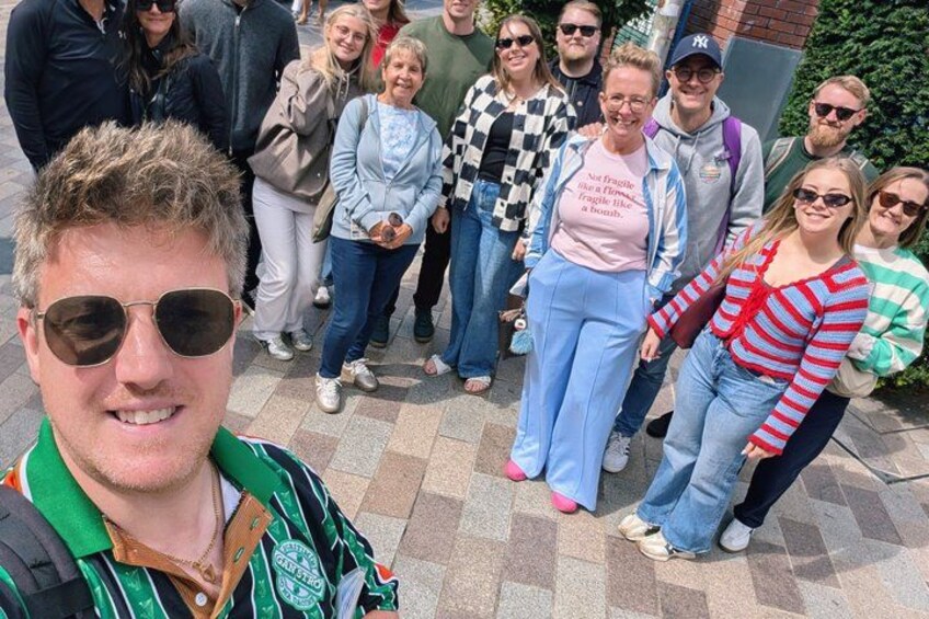 A group of people standing outdoors on a paved area with a brick wall in the background. 3
