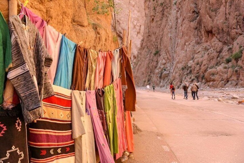 Colorful textiles hanging on a line, a rocky cliff, and a road with people in the distance. 2