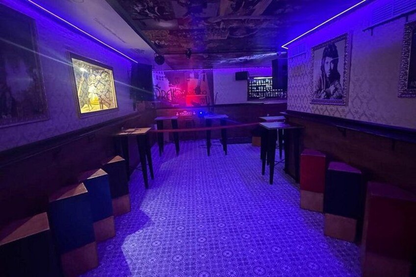 A dimly lit room with patterned flooring, tables, and chairs arranged for seating. 2