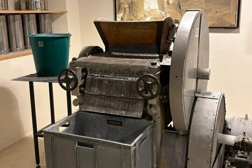 Une machine industrielle ancienne, dotée d’une grande roue, d’une trémie et d’un récipient en métal. 4