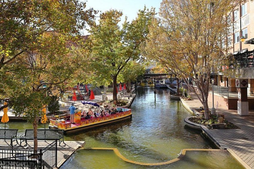 A canal with a boat carrying passengers, surrounded by trees and buildings. 2