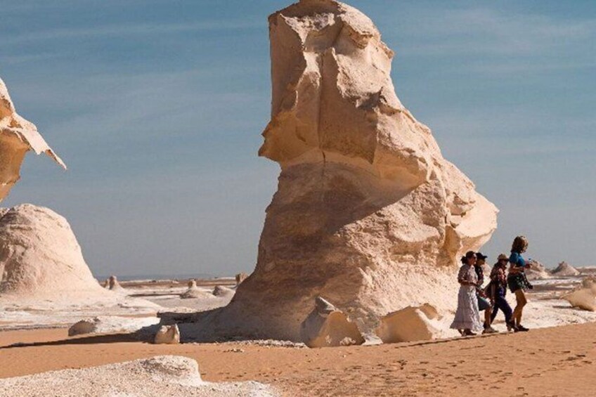 A desert landscape with large rock formations and a group of people standing near the base of one formation. 1