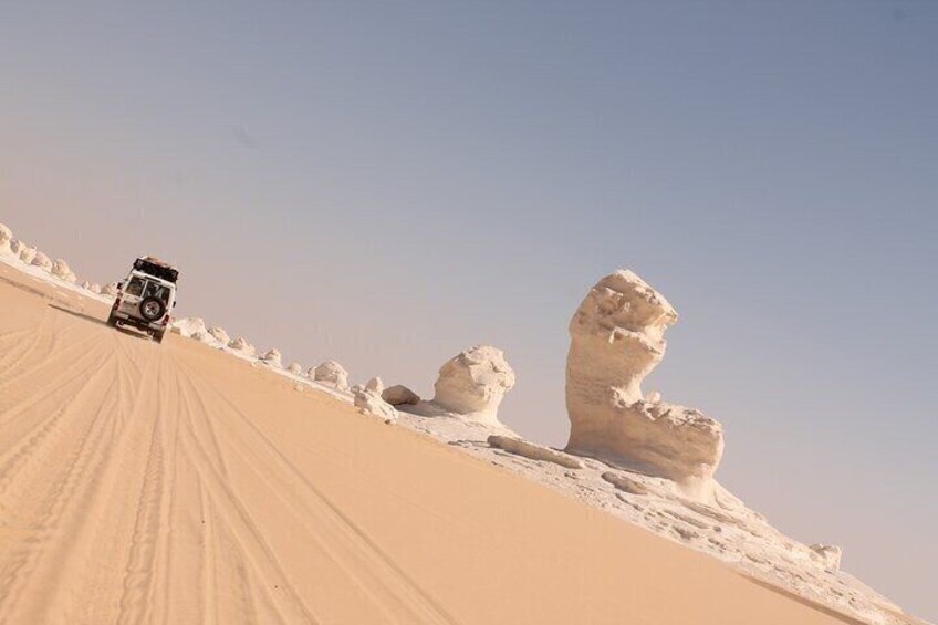 A vehicle on a sandy dune with a large rock formation resembling a head. 4