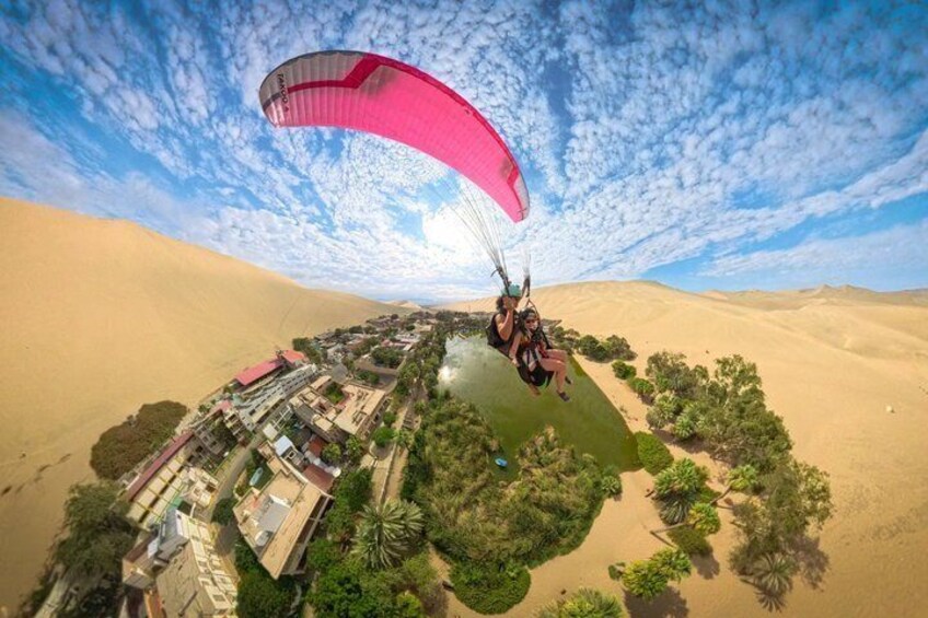 A person paragliding over a desert landscape with buildings and greenery below. 3