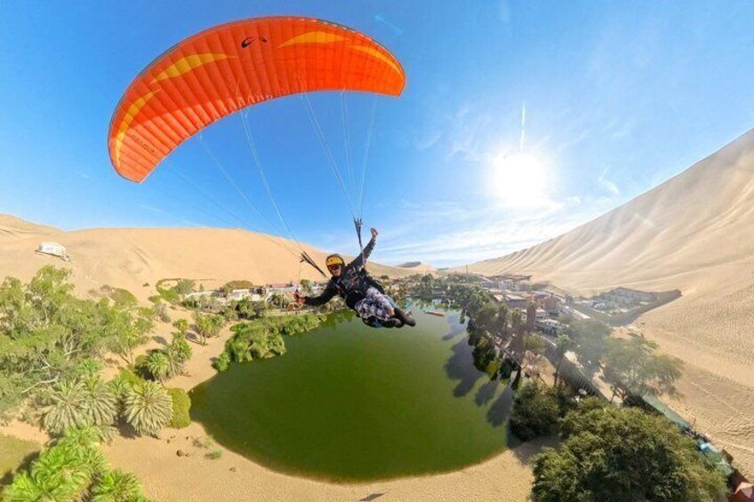A paragliding scene over a desert landscape with sand dunes and sparse vegetation. 2