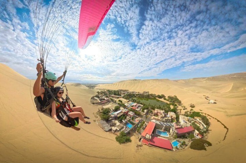 A person paragliding over a desert landscape with a small settlement below. 1