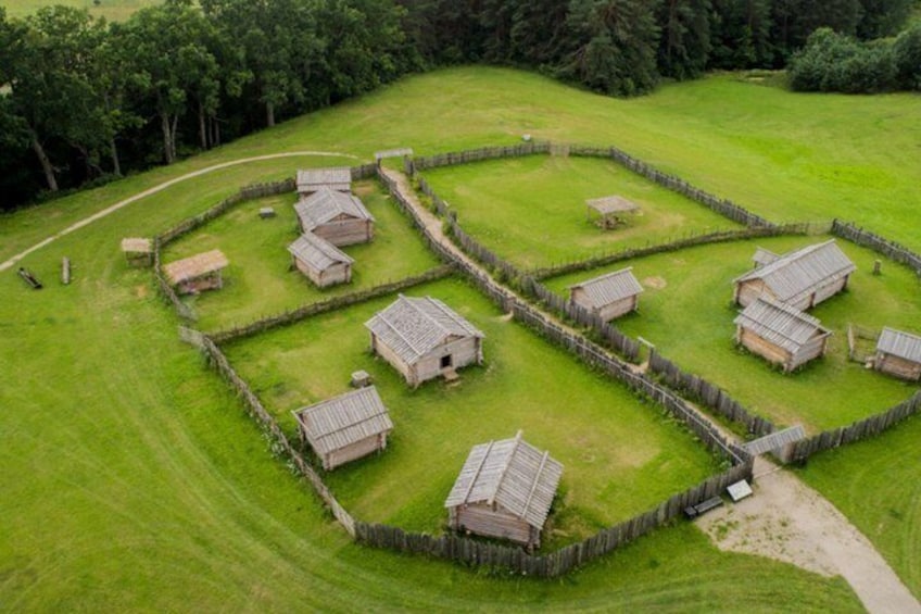 A rural landscape with a series of stone buildings arranged in a circular pattern, surrounded by a wooden fence. 5