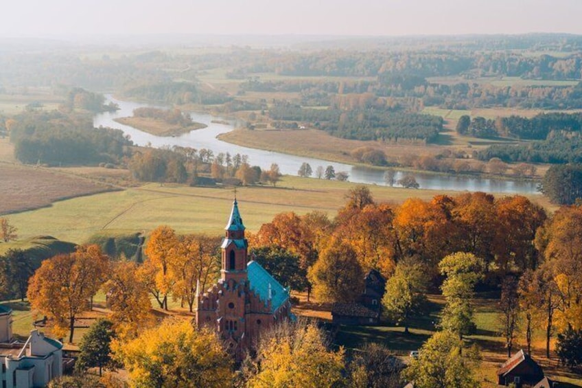A church with a blue roof, surrounded by autumn-colored trees and a river in the background. 1