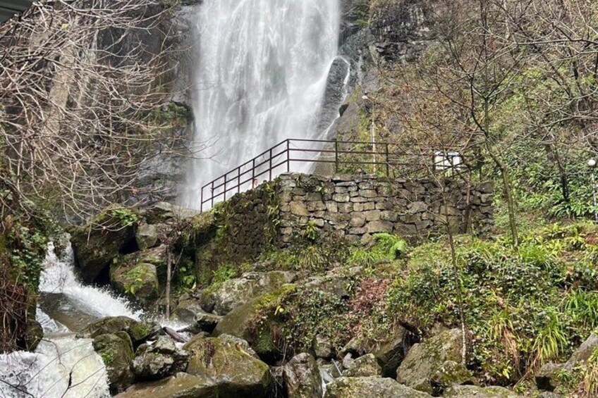 Une cascade d’eau dévalant des rochers, un pont de pierre et une végétation luxuriante tout autour. 2