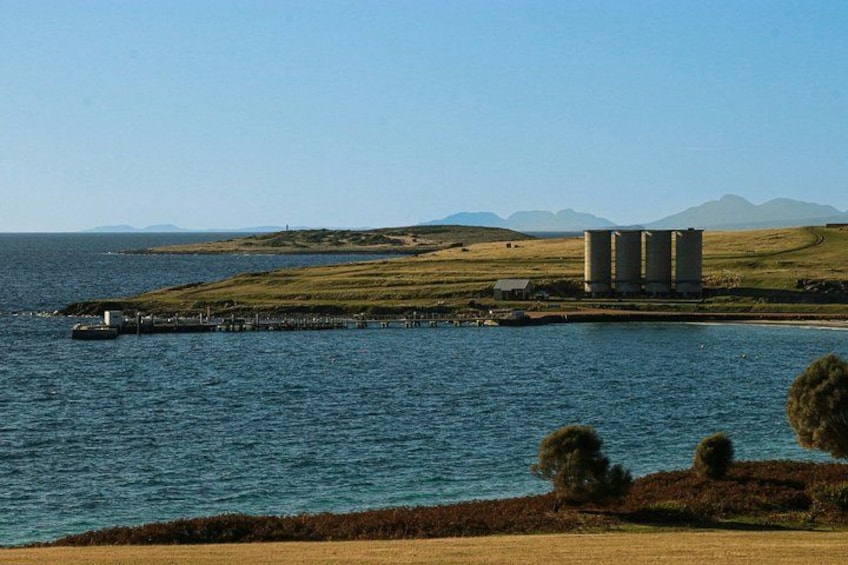 A coastal landscape with a dock, a lighthouse, and storage silos. 1