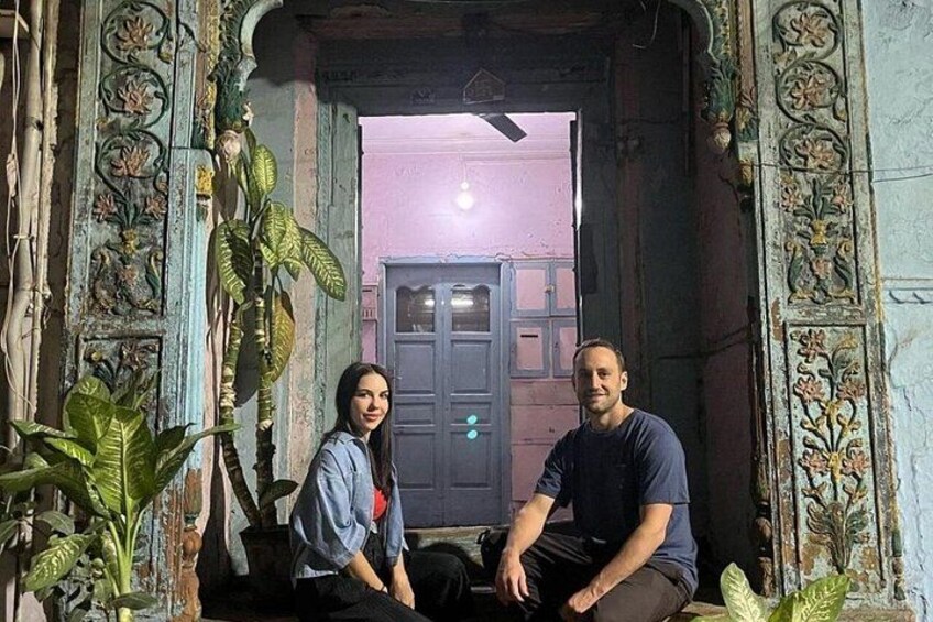 Two people sitting in an ornate doorway with intricate carvings and a plant on the left. 4