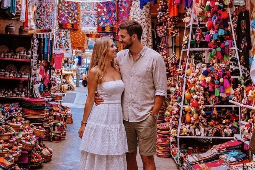 A couple standing in a market with colorful textiles and crafts. 1