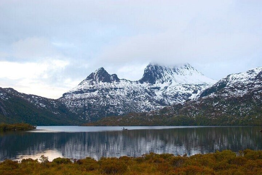 A mountain range with snow-capped peaks, a calm lake, and a forested foreground. 1