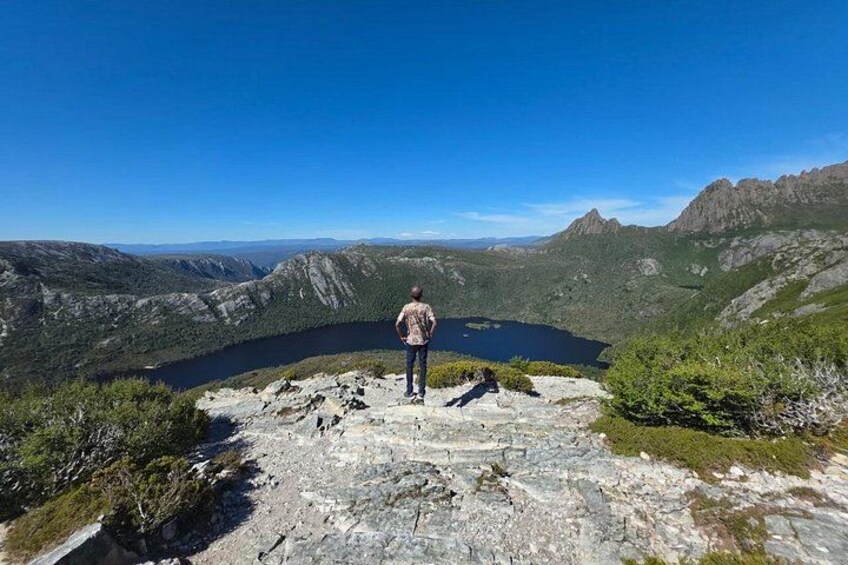 A person standing on a rocky outcrop overlooking a lake surrounded by mountains. 2