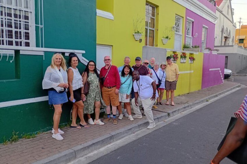 A group of people standing on a sidewalk next to colorful buildings. 1