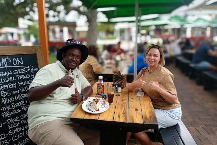 Two people sitting at an outdoor table with a menu board behind them. 2