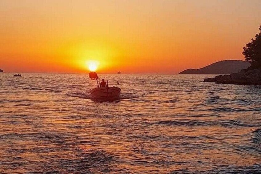 A sunset over a calm sea with a boat carrying people. 2